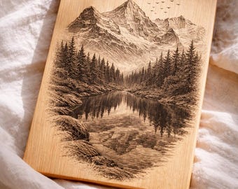May include: A rectangular wooden plaque featuring a detailed engraving of a mountain landscape with a lake and forest. The artwork is in shades of brown and black, with birds flying in the sky. The plaque is resting on a white, textured surface.