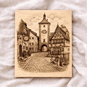 Può includere: Pannello in legno color seppia con un'incisione di una piazza europea. L'opera mostra una strada acciottolata che conduce a un campanile e ad edifici con dettagli architettonici. Un orologio è visibile sulla facciata di un edificio.