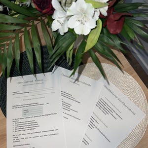 May include: A bouquet of white and burgundy flowers with green leaves, next to printed papers with German text. The papers appear to be related to a school event, with headings like "Elternabend-Klasse" and "Checkliste für den Elternabend."