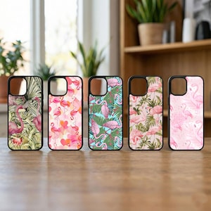 May include: Five phone cases with black borders, each featuring a different flamingo design. The cases display pink flamingos with tropical foliage, hearts, and geometric patterns. The cases are arranged on a wooden surface.
