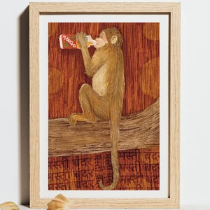 May include: A framed print depicting a monkey drinking from a bottle labelled "Mango." The monkey is perched on a branch against a reddish-brown background. The print has text at the bottom and is in a light wood frame.