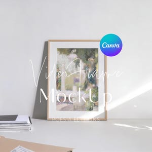 May include: A vertical rectangular picture frame with a light wood finish containing an impressionistic painting of a garden scene with trees and white structures. The text Canva is in a blue and purple circle in the upper right corner.