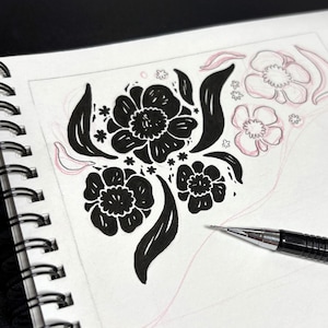 May include: A spiral-bound sketchbook page featuring a black ink floral illustration with three prominent flowers and leaves, alongside light pink pencil sketches of additional flowers and a mechanical pencil resting on the paper with the text whee.