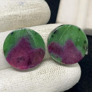 Peut inclure: Deux pierres précieuses rondes avec un motif de couleur vert et magenta. Les pierres précieuses sont polies et semblent être des pierres naturelles. Les pierres précieuses sont présentées sur une surface blanche.
