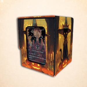 May include: A rectangular card storage box featuring a black cat wearing a witch hat, surrounded by glowing orange jack-o'-lanterns and candles. A clear window on the front displays a Magic: The Gathering card titled Raugrin Triome.