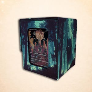 May include: A rectangular deck box featuring a dark forest scene with a wolf silhouette and a clear window displaying a Raugrin Triome trading card. The exterior has a black border and a printed design of trees in shades of teal and dark green.
