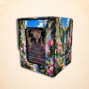May include: A rectangular deck box featuring a vibrant, full-color print of a lush garden path with pink flowers, stone arches, and a blue sky. A clear window on the front displays a Savai Triome trading card with text including Land, Island, Mountain, Plains.