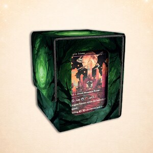 Könnte beinhalten: Eine quadratische Deckbox mit einem dunkelgrünen Waldmotiv und einem zentralen rechteckigen Sichtfenster, in dem eine Sammelkarte liegt. Die Karte zeigt eine Landschaftsillustration mit einem großen Mond und hohen Kristallstrukturen.