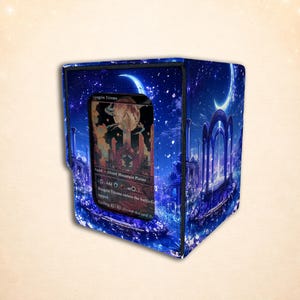 May include: A blue rectangular deck box featuring a fantasy landscape with a crescent moon and stone arches. A clear window on the front displays a Magic: The Gathering card titled Raugrin Triome, which depicts a glowing landscape and a large moon.