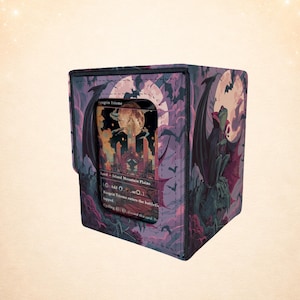 Puede incluir: Una caja de almacenamiento de cartas morada con una ilustración de fantasía de un vampiro y una luna llena. La caja tiene una ventana transparente que muestra una carta con el texto "Angrin Triome". La caja está decorada con murciélagos y un estampado floral.
