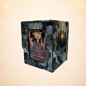 Puede incluir: Una caja de almacenamiento de cartas con un diseño oscuro y estampado con nubes y una gran flor de loto. La caja contiene una carta con el texto "Angrin Triome" y una ilustración de paisaje. Diseñado para proteger y almacenar cartas coleccionables.