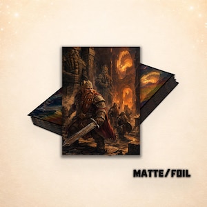 May include: A stack of rectangular art prints featuring a fantasy scene with a bearded warrior in armor holding a sword, standing before stone statues and a fiery background. The text MATTE/FOIL is printed in black in the lower right corner.