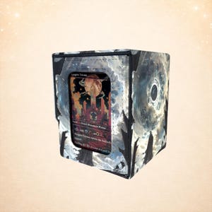 Puede incluir: Una caja de almacenamiento de tarjetas en blanco y negro con un diseño de galaxia pintada. La caja tiene una ventana transparente que muestra una tarjeta con el texto "Anguish Triome". La tarjeta presenta un paisaje de fantasía con una gran luna.