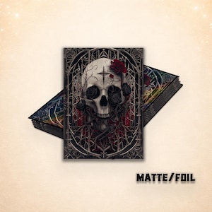 May include: A rectangular print featuring a central skull illustration adorned with dark roses and a small cross symbol, set against an intricate gothic-style frame. The artwork displays a matte and foil finish with the text MATTE/FOIL visible below.