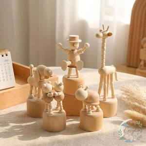 Puede incluir: Una colección de figuras de animales de madera, incluyendo una jirafa, un perro, un oso y una vaca. Las figuras son de color marrón claro y se asientan sobre bases redondas o cuadradas. También se presenta un hombre de madera con sombrero.
