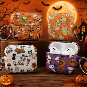 May include: Four protective cases for wireless earbuds featuring Snoopy and Halloween-themed graphics. The cases include orange, white, and purple designs with pumpkins, ghosts, and bats. Each case has a metal ring attachment for carrying.