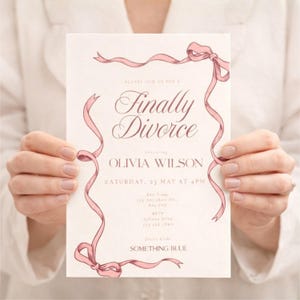 Könnte beinhalten: Eine cremefarbene Einladung mit rosa Schleifen und dem Schriftzug "Finally Divorce" in eleganter Schrift. Die Einladung enthält Details für Olivias Veranstaltung, einschließlich Datum, Uhrzeit und Kleiderordnung: "Something Blue."