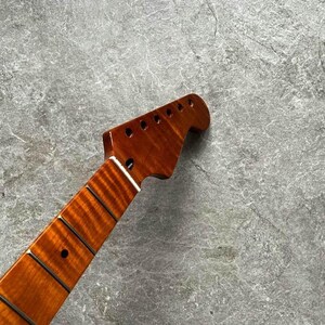 May include: A close-up of a guitar neck with a rich, reddish-brown finish. The headstock features six tuning peg holes. The fretboard has dark frets and inlaid position markers. The wood grain is visible, adding to the instrument's aesthetic.