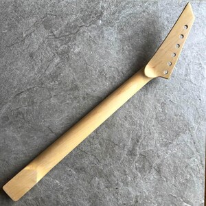 May include: A light-colored, unfinished guitar neck with a headstock featuring seven tuning peg holes. The neck is made of wood and is ready for customization. The design is simple and classic, perfect for guitar builders.