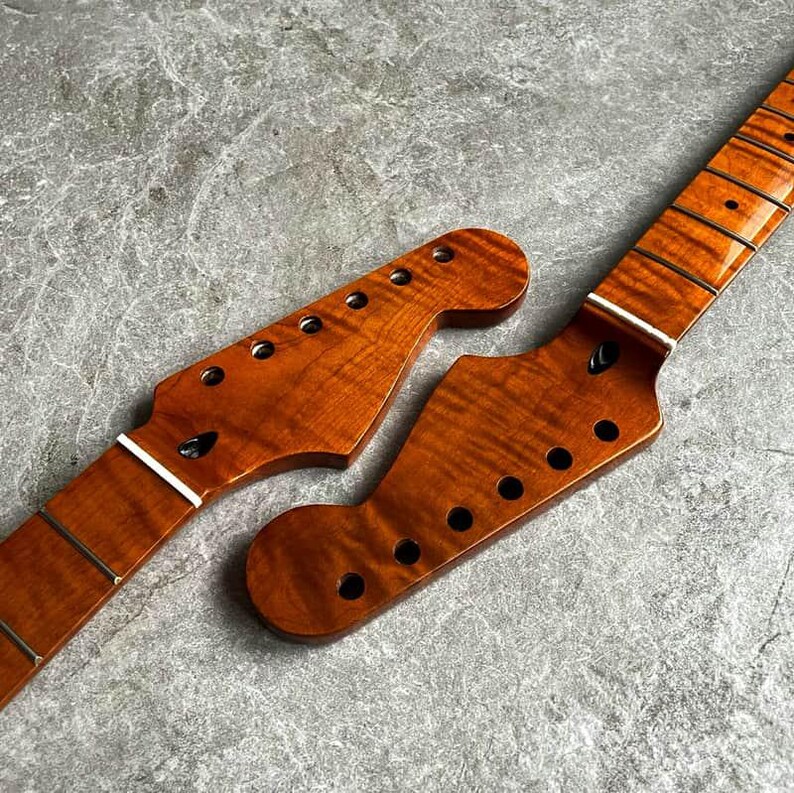 May include: Two unfinished guitar necks with a flamed maple grain pattern. The necks are a warm amber color, with pre-drilled holes for tuning pegs and frets. The headstocks have a classic shape.