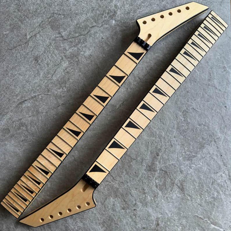 May include: Two unfinished guitar necks with light wood and black fret markers. The necks have a natural wood finish and are angled, with tuning peg holes at the headstock. The fretboards have black triangular inlays.