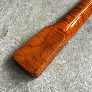 May include: Close-up of a wooden object with a glossy finish. The wood grain is visible, showcasing a rich, reddish-brown color. The object has a rectangular shape with rounded edges, and a smooth, polished surface.