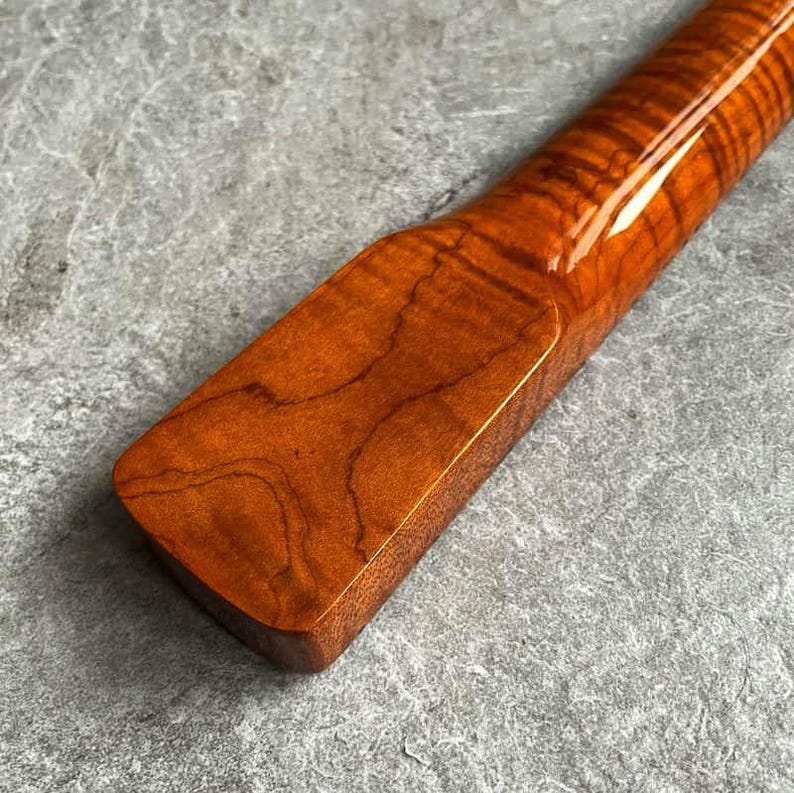 May include: Close-up of a wooden object with a glossy finish. The wood grain is visible, showcasing a rich, reddish-brown color. The object has a rectangular shape with rounded edges, and a smooth, polished surface.