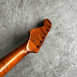 May include: Close-up of a guitar neck and headstock. The wood has a rich, warm brown color with a glossy finish. Six black tuning pegs are visible on the headstock. The wood grain has a unique, swirling pattern.