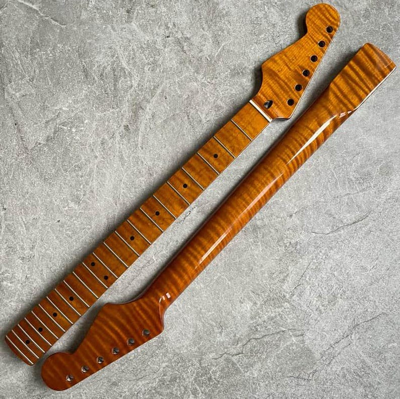 K&ouml;nnte beinhalten: Zwei unfertige Gitarrenh&auml;lse mit geflammtem Ahornmuster. Die H&auml;lse sind warm bernsteinfarben, mit Bundmarkierungen und L&ouml;chern f&uuml;r die Stimmwirbel. Einer ist abgewinkelt, der andere gerade.