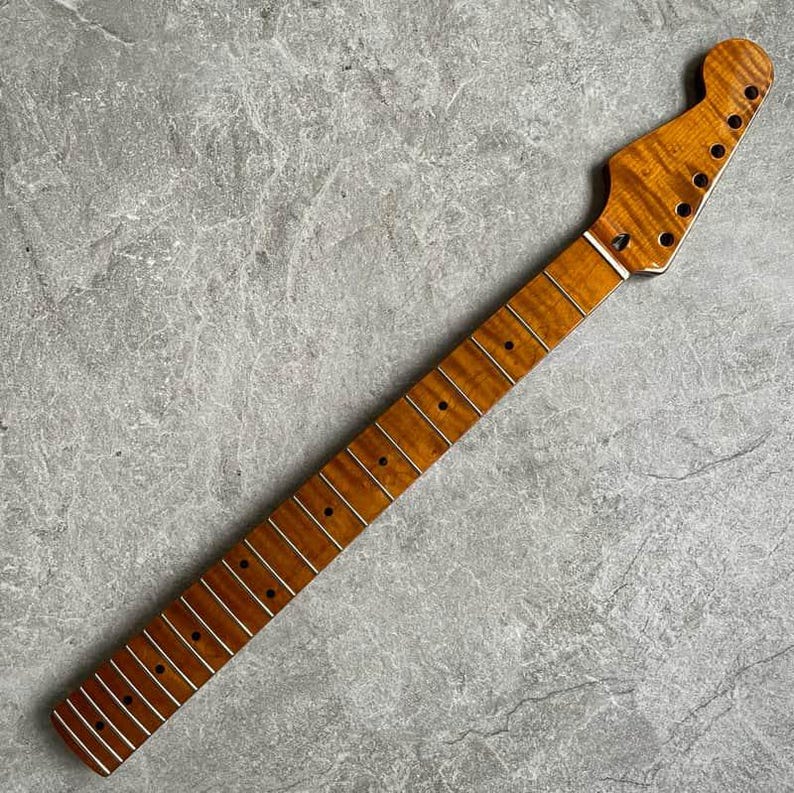 K&ouml;nnte beinhalten: Ein Gitarrenhals mit geflammter Ahorn-Oberfl&auml;che. Der Hals ist hellbraun mit dunkelbraunen Bundmarkierungen und silbernen B&uuml;nden. Die Kopfplatte hat L&ouml;cher f&uuml;r die Stimmwirbel.