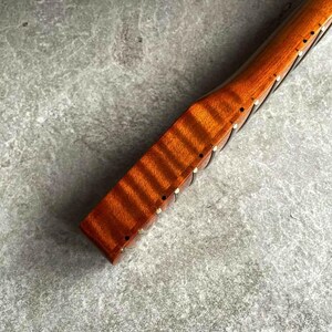May include: Close-up of a wooden instrument neck with a rich, reddish-brown finish. The wood grain is visible, and small, inlaid markers are present along the neck. The instrument appears to be a stringed instrument, possibly a guitar or violin.
