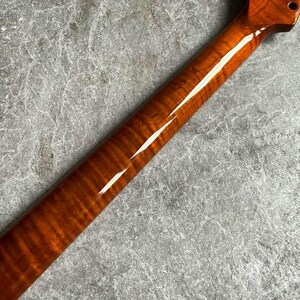 May include: A close-up of a guitar neck with a glossy, amber-colored finish. The wood grain is visible, creating a striped pattern. The headstock has a single tuning peg hole.