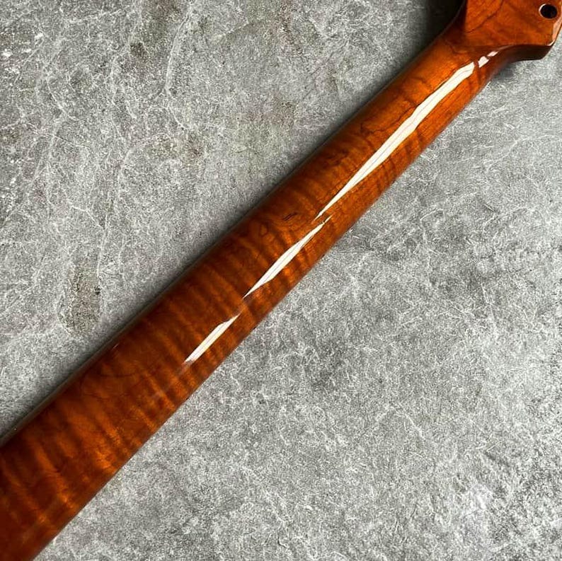 May include: A close-up of a guitar neck with a glossy, amber-colored finish. The wood grain is visible, creating a striped pattern. The headstock has a single tuning peg hole.