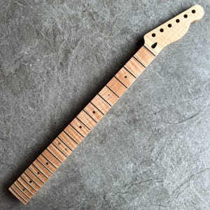 May include: A new, unfinished guitar neck with a natural wood finish. The neck features a headstock with pre-drilled holes for tuning pegs and a fretboard with inlaid fret markers. The wood grain is visible throughout the neck.