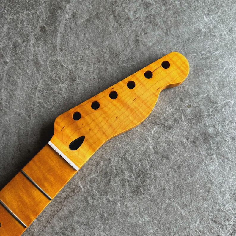 May include: Close-up of a guitar neck with a natural wood finish. The headstock features six black tuning peg holes. The fretboard has metal frets. The wood grain is visible, showing a light brown and yellow color.