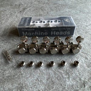 May include: A set of six silver-colored metal guitar machine heads with tuning pegs, six matching circular metal ferrules, and a small clear plastic bag containing six mounting screws, all presented with a box labeled Professional Machine Heads.