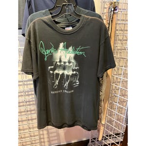 May include: A white ceramic mug with a black handle and the text "But First, Coffee" in a black, bold font. The mug is on a wooden surface. The mug is 10 cm tall.