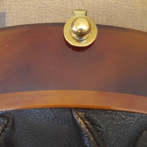 Puede incluir: Un bolso vintage con la parte superior de color marr&oacute;n carey y la parte inferior de cuero negro. El bolso tiene un cierre de metal dorado con un pomo redondo.