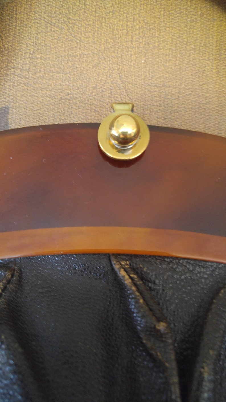 Puede incluir: Un bolso vintage con la parte superior de color marr&oacute;n carey y la parte inferior de cuero negro. El bolso tiene un cierre de metal dorado con un pomo redondo.