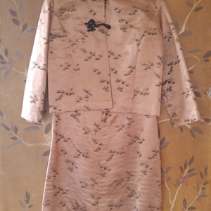 May include: A vintage pink satin dress with a matching jacket. The dress and jacket feature a black bird print pattern. The jacket has a mandarin collar and black button closures.