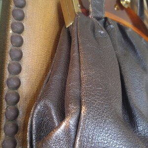Puede incluir: Un bolso de mano de cuero marr&oacute;n con asa superior y cierre dorado. El bolso tiene una forma redondeada y un exterior de cuero texturizado.