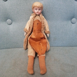 1890s antique blonde China head doll with stuffed body and leather apron and long leather coat. 9 inches