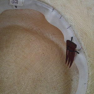 May include: The inside of a straw hat with a white ribbon and a brown comb attached to the ribbon. The hat is made of woven straw and has a label that says "22" on it.