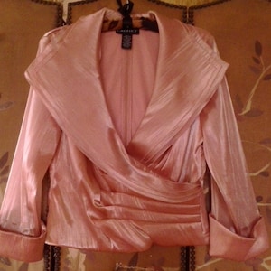 May include: A long-sleeved, blush-colored satin blouse with a draped, cowl neckline and a gathered waist. The blouse has a label that reads "Cachet" on the inside collar.