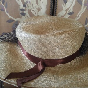 May include: A wide-brimmed straw hat with a brown ribbon tied around the crown. The hat is light brown and has a woven texture.