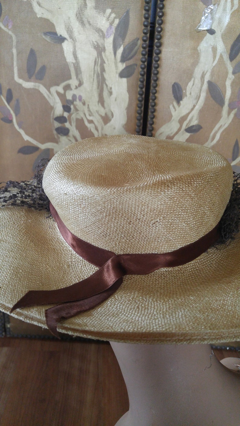 May include: A wide-brimmed straw hat with a brown ribbon tied around the crown. The hat is light brown and has a woven texture.