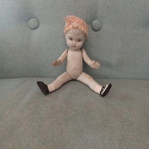 Antique porcelain jointed limbs doll with painted face, socks and shoes. Molded hair, in pink bonnet. Made in japan 1920s