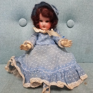 Antique Heubach Koppelsdorf little bisque doll with dark wig, glass eyes wearing a blue polka dot dress and bonnet