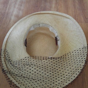 May include: A straw hat with a black netting trim. The hat is light brown and has a wide brim.