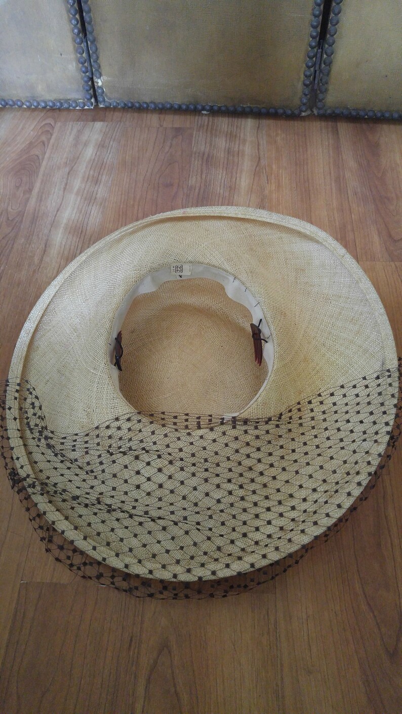 May include: A straw hat with a black netting trim. The hat is light brown and has a wide brim.